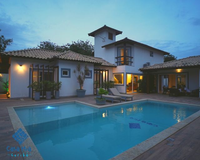 Fachada da Casa Mia ao entardecer, com a piscina iluminada